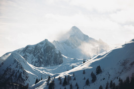 Morgenstimmung auf den verschneiten Bergen rund um das Kitzsteinhorn, mit prominenter Gipfelform im Hintergrund, bewölktem Himmel und schneebedeckten Hängen.