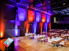 Veranstaltungssaal mit Tischen und Stühlen vor Bühne © Putz & Stingl Veranstaltungssaal mit Tischen und Stühlen vor Bühne